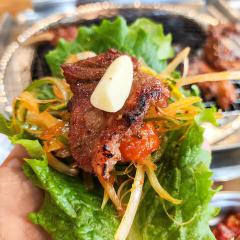 Hand holding Korean BBQ Galbi (Grilled Ribs) lettuce wrap with garlic and green onion salad